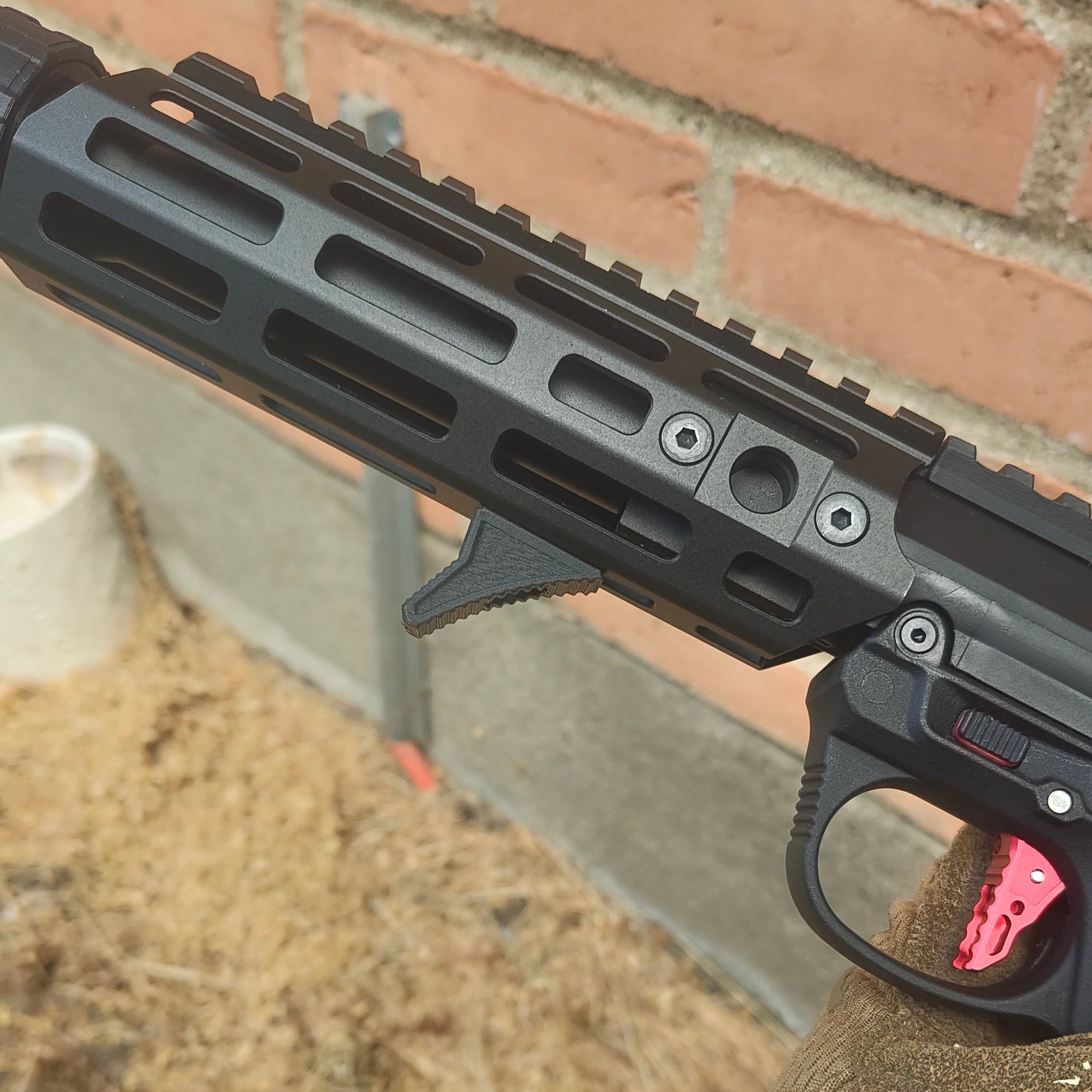 Close-up of a person holding a black firearm with a pink trigger, outdoors.